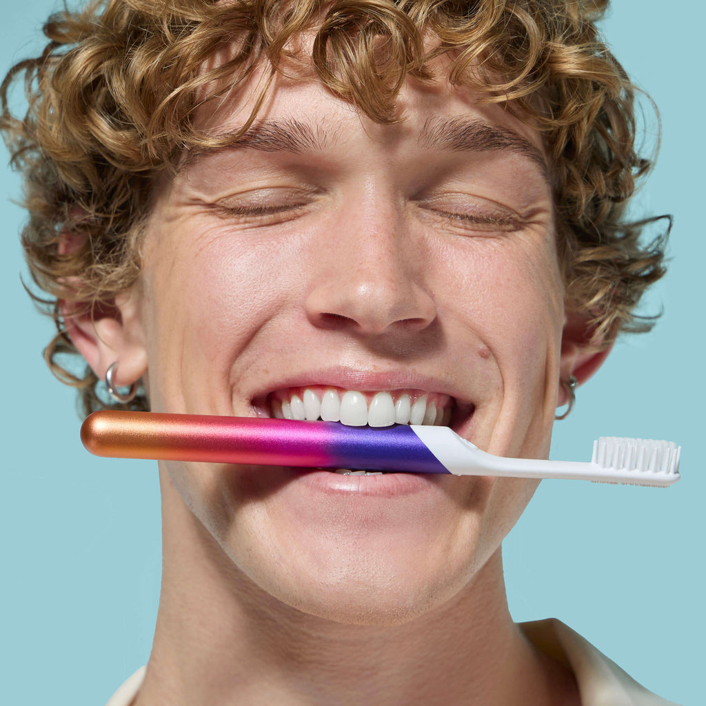 Person with a colorful toothbrush in their mouth against a light blue background