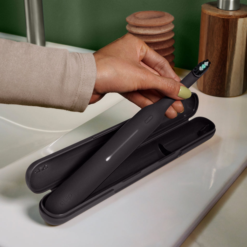Ultra™ Travel Case holding a sleek black electric toothbrush, shown open on a bathroom counter as a hand lifts the toothbrush from the protective case.