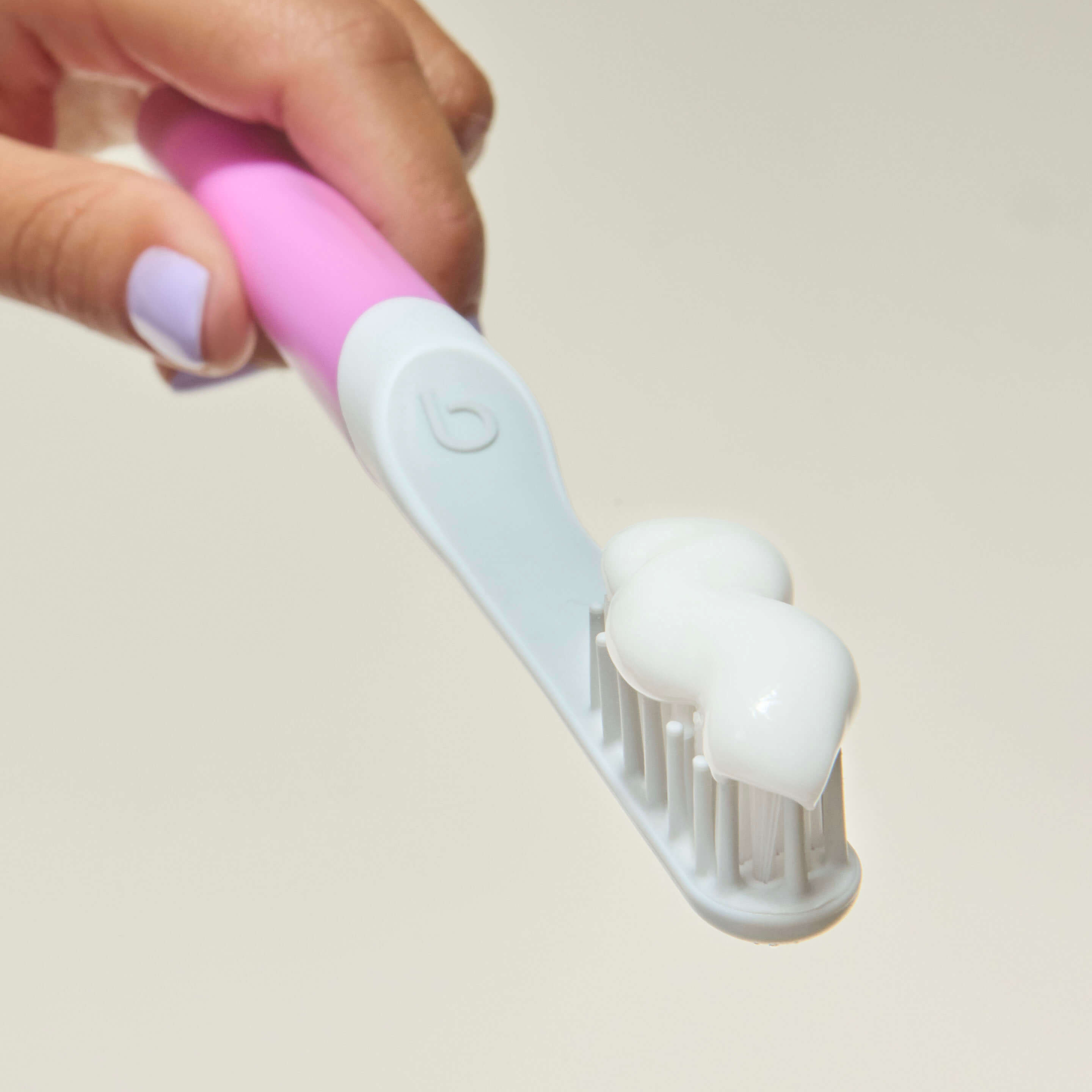 Hand holding a pink and white toothbrush against a plain background