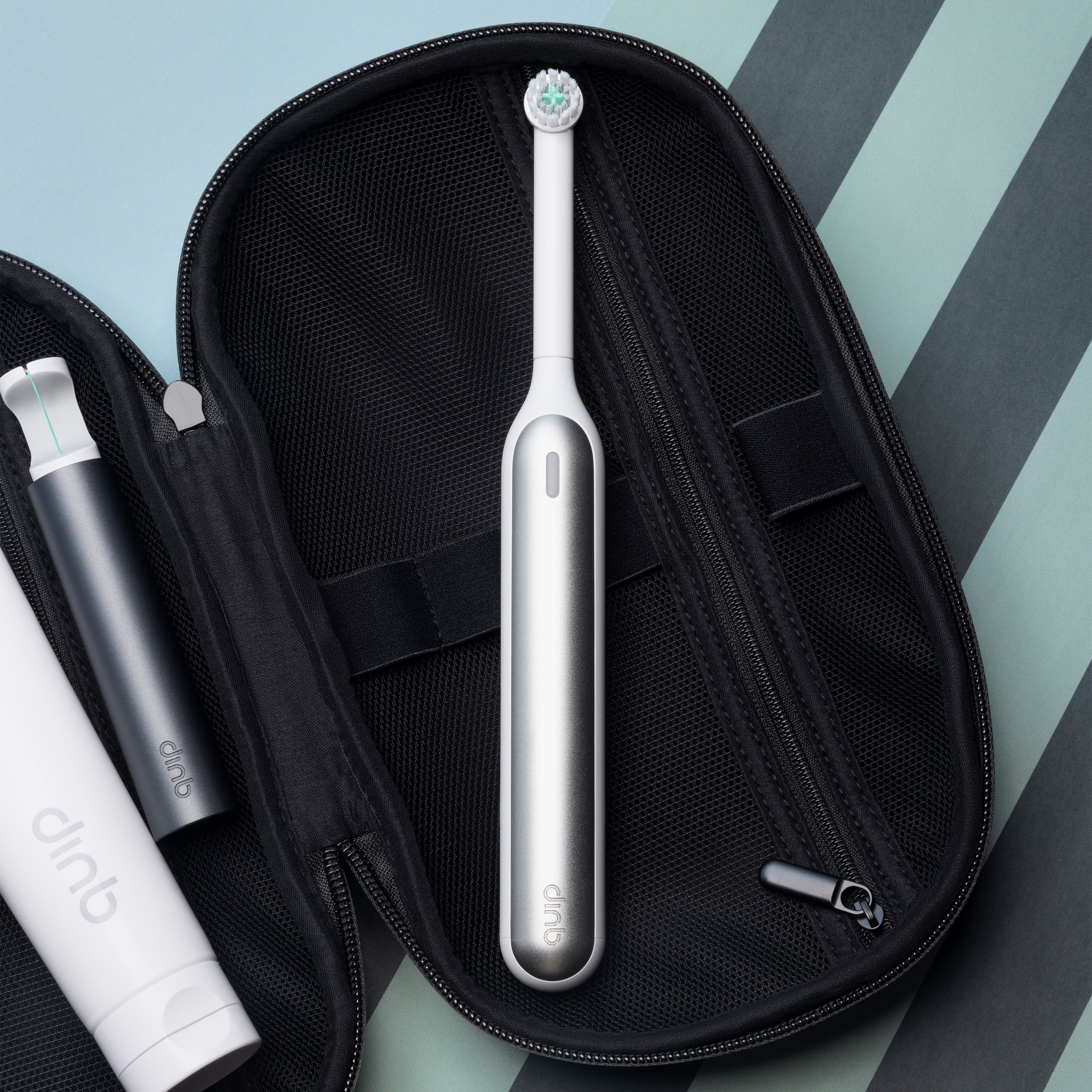 Silver Quip electric toothbrush shown inside an open black travel case with other oral-care items.