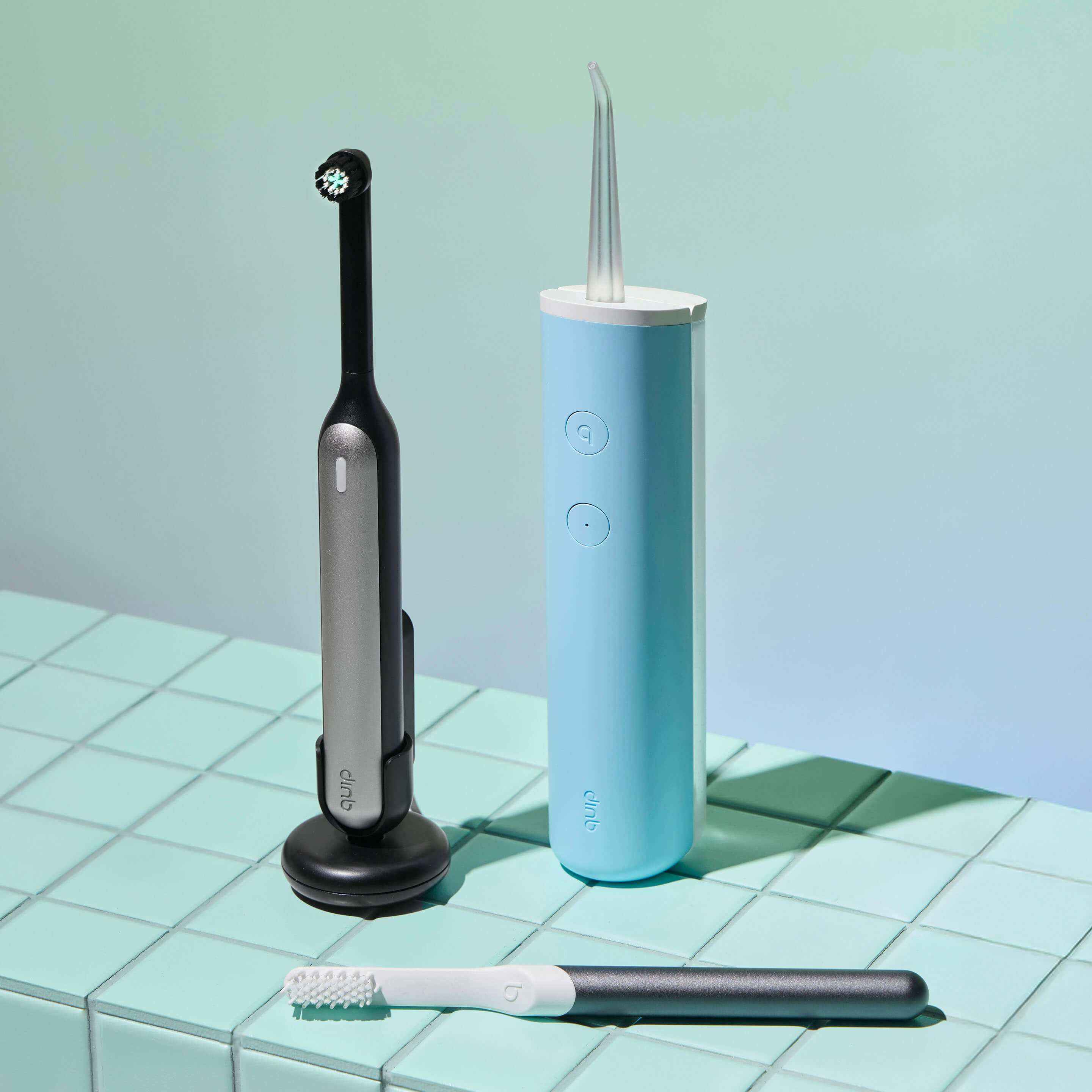 Quip dental tools including a black electric toothbrush, blue water flosser, and white brush on a green tiled surface.