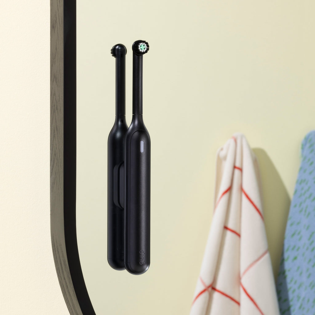 Two black electric toothbrushes hanging on a magnetic strip against a beige wall.