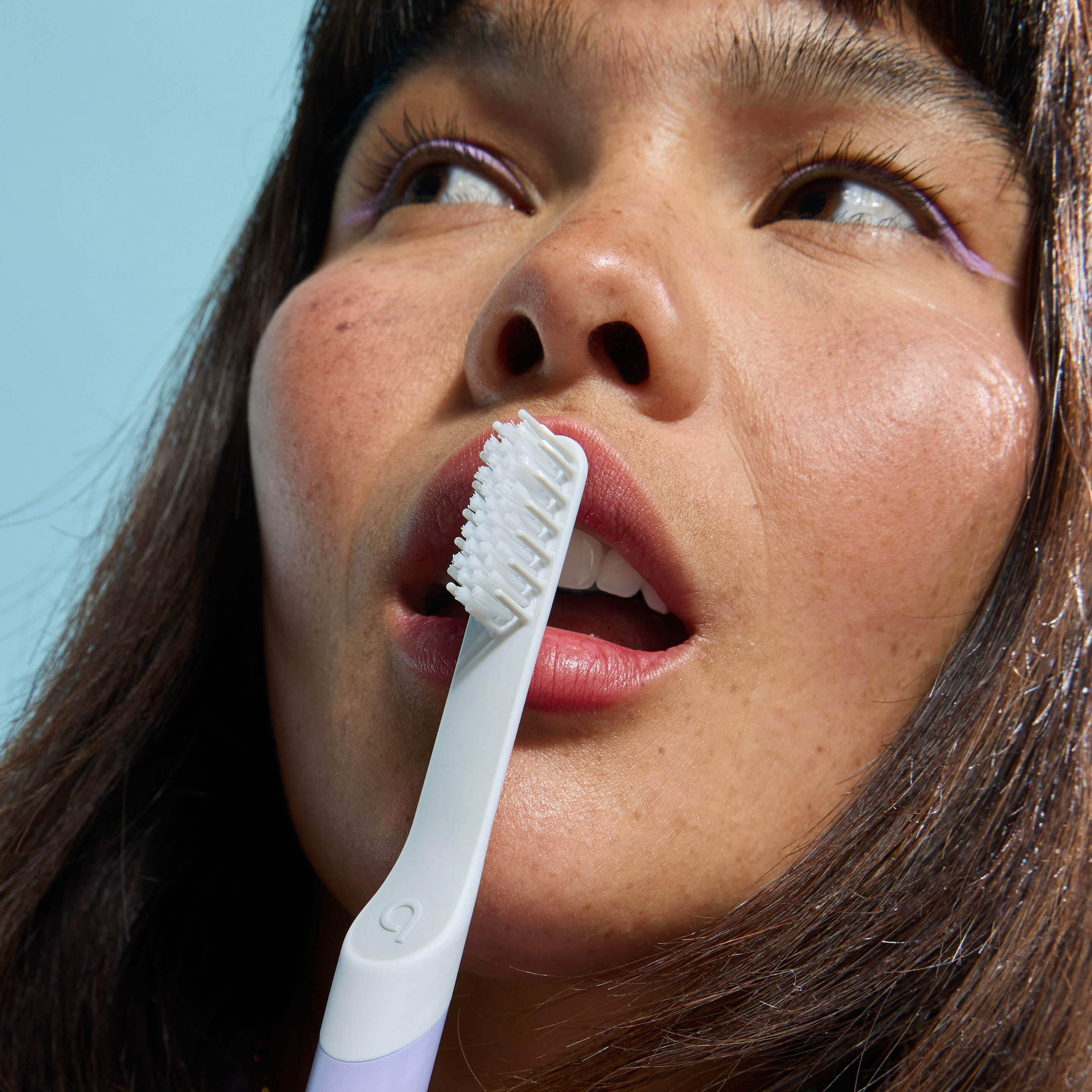 Person brushing their teeth with a white toothbrush against a light blue background