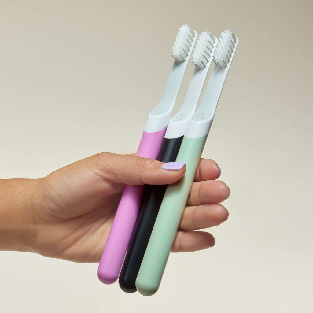 Hand holding three colorful toothbrushes against a plain background