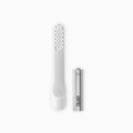 An image showing a white toothbrush head refill with soft bristles and a tongue scraper, accompanied by a AAA battery.