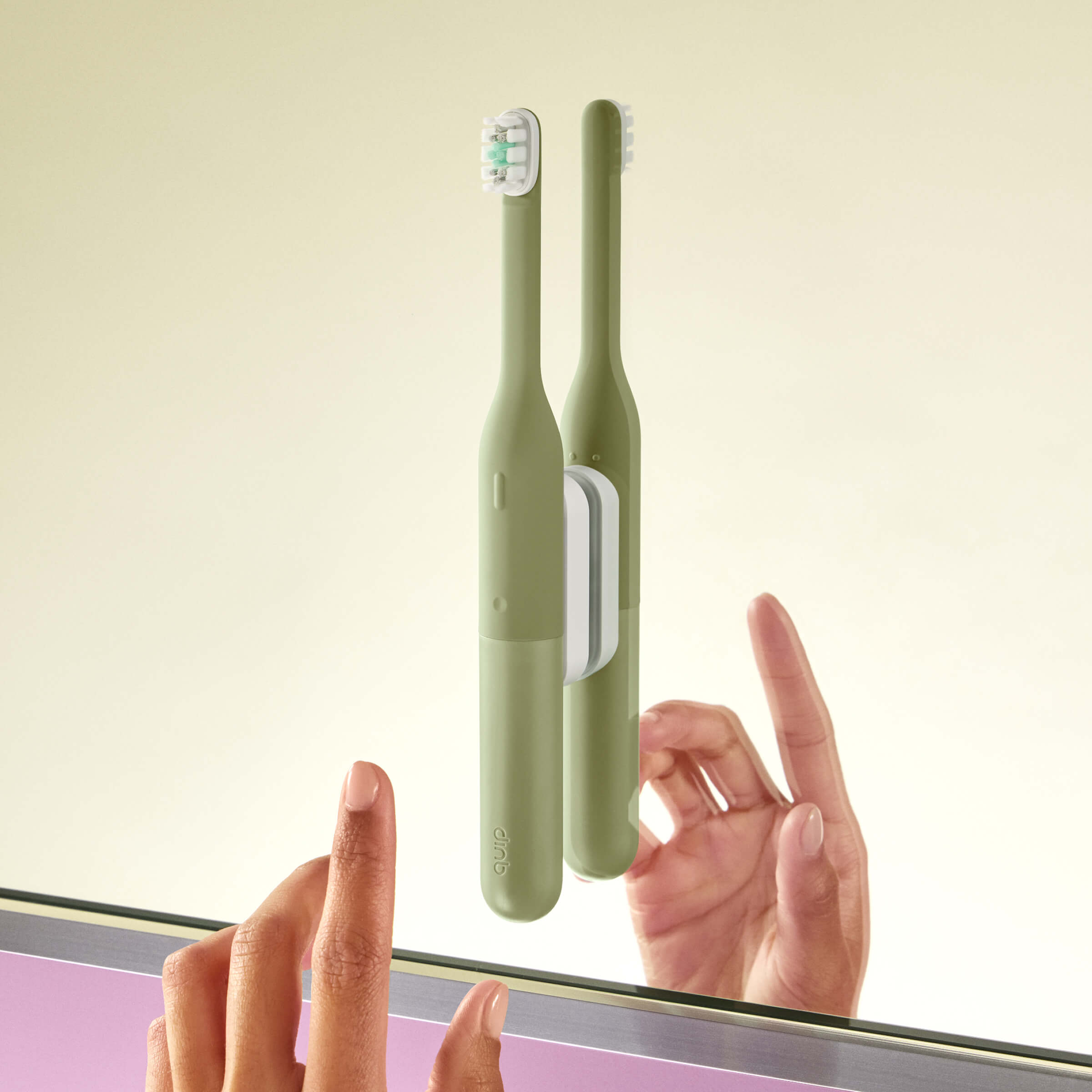 Two green electric toothbrushes with a holder on a light beige background
