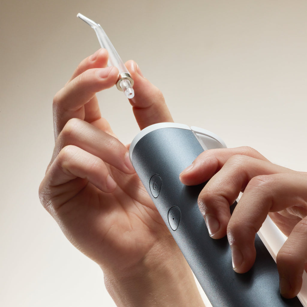 Close-up of hands attaching a clear angled tip to a handheld water flosser device with a dark handle and control buttons.