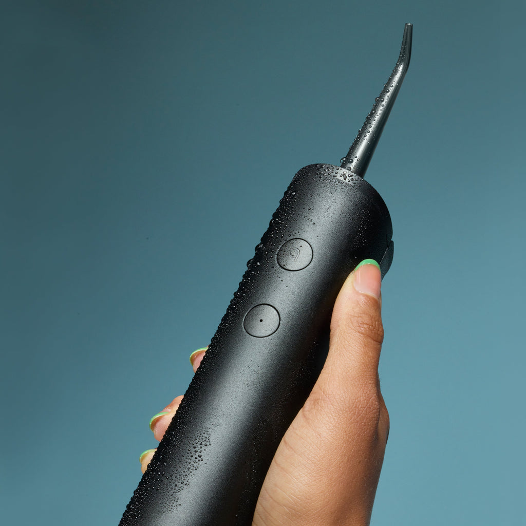 Hand holding a black quip Water Flosser with water droplets on the surface.
