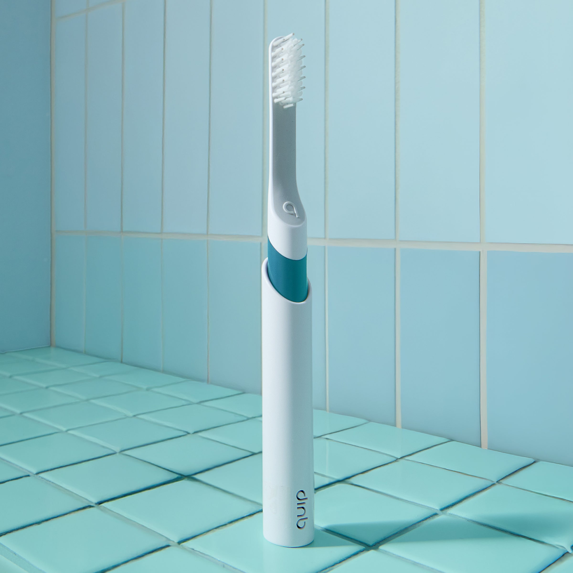 White and blue electric toothbrush on a tiled bathroom floor with a light blue wall.