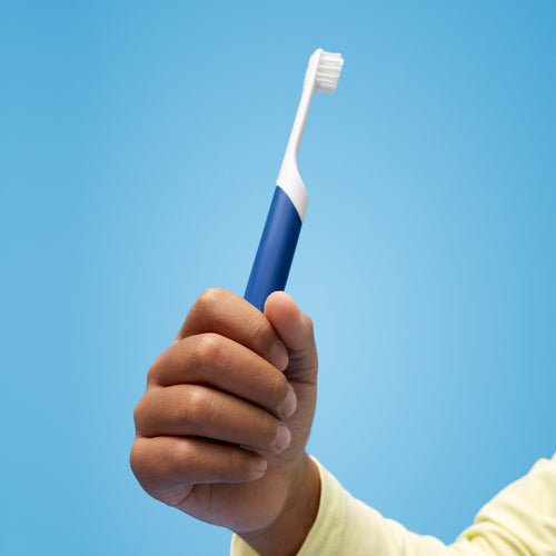 A child’s hand holding a blue quip Kids Sonic toothbrush against a bright blue background.