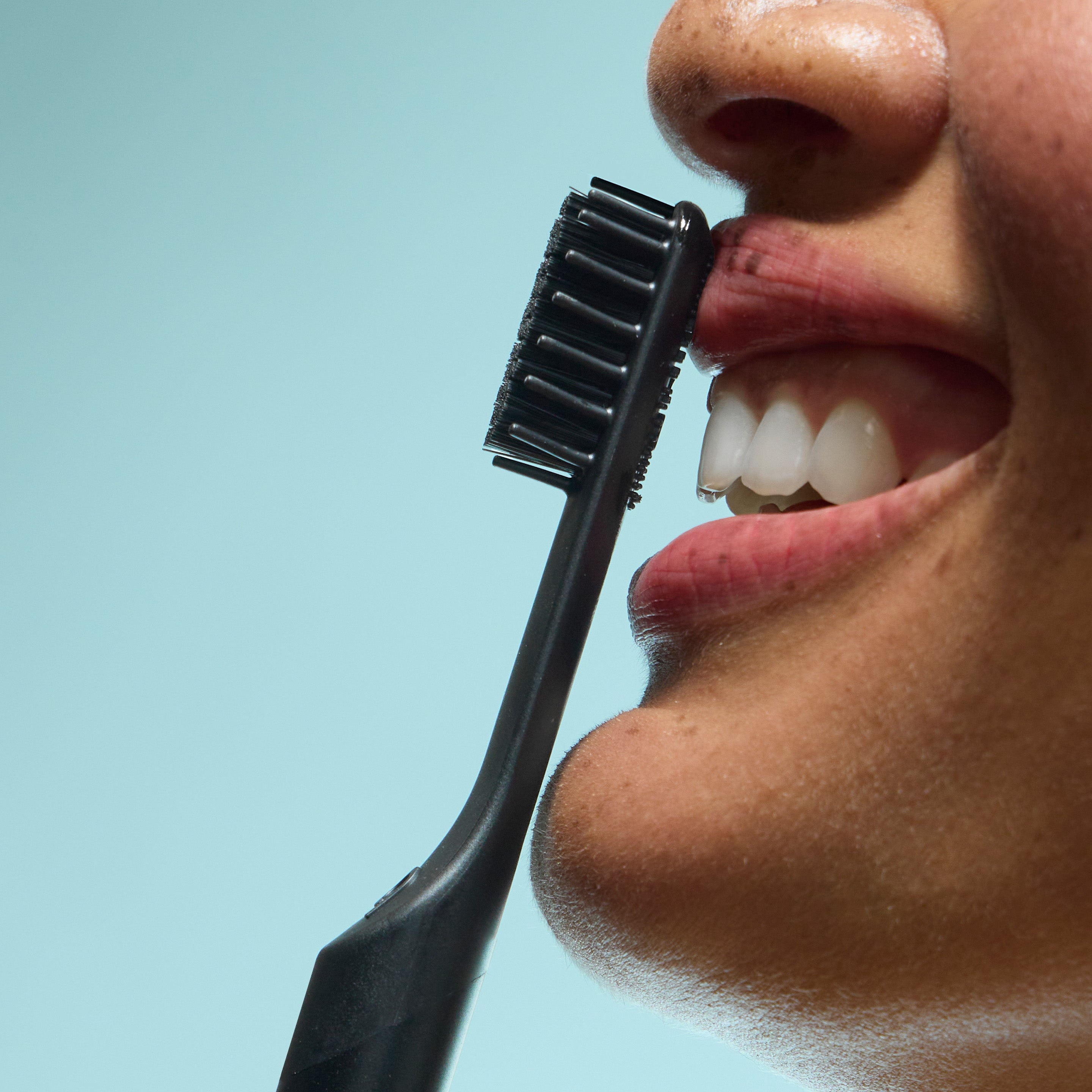 Person smiling as a black toothbrush is held near their teeth.