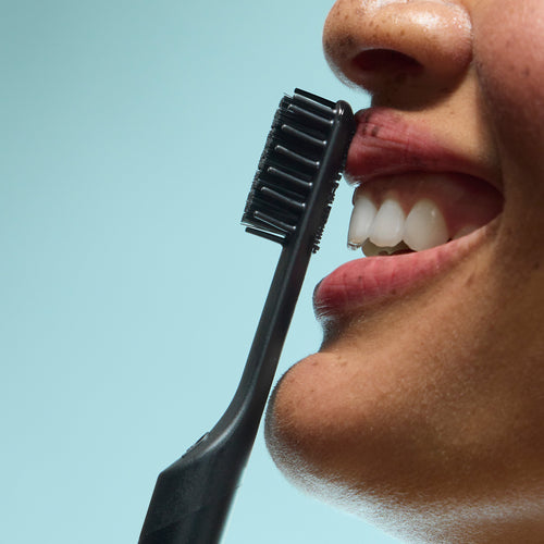 Person smiling as a black toothbrush is held near their teeth.